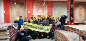 Foto di gruppo con lo striscione YellowTheWorld davanti ai tappeti appesi alle pareti